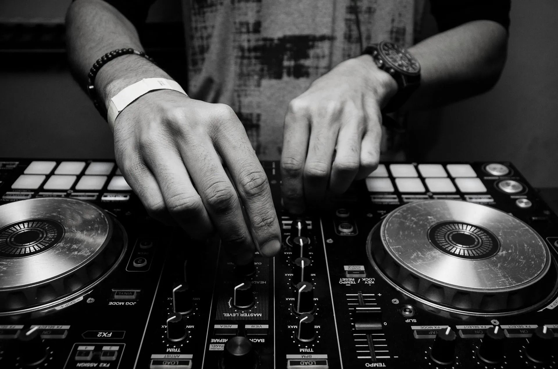 Hands adjusting controls on a DJ mixer with turntables in a black-and-white scene
