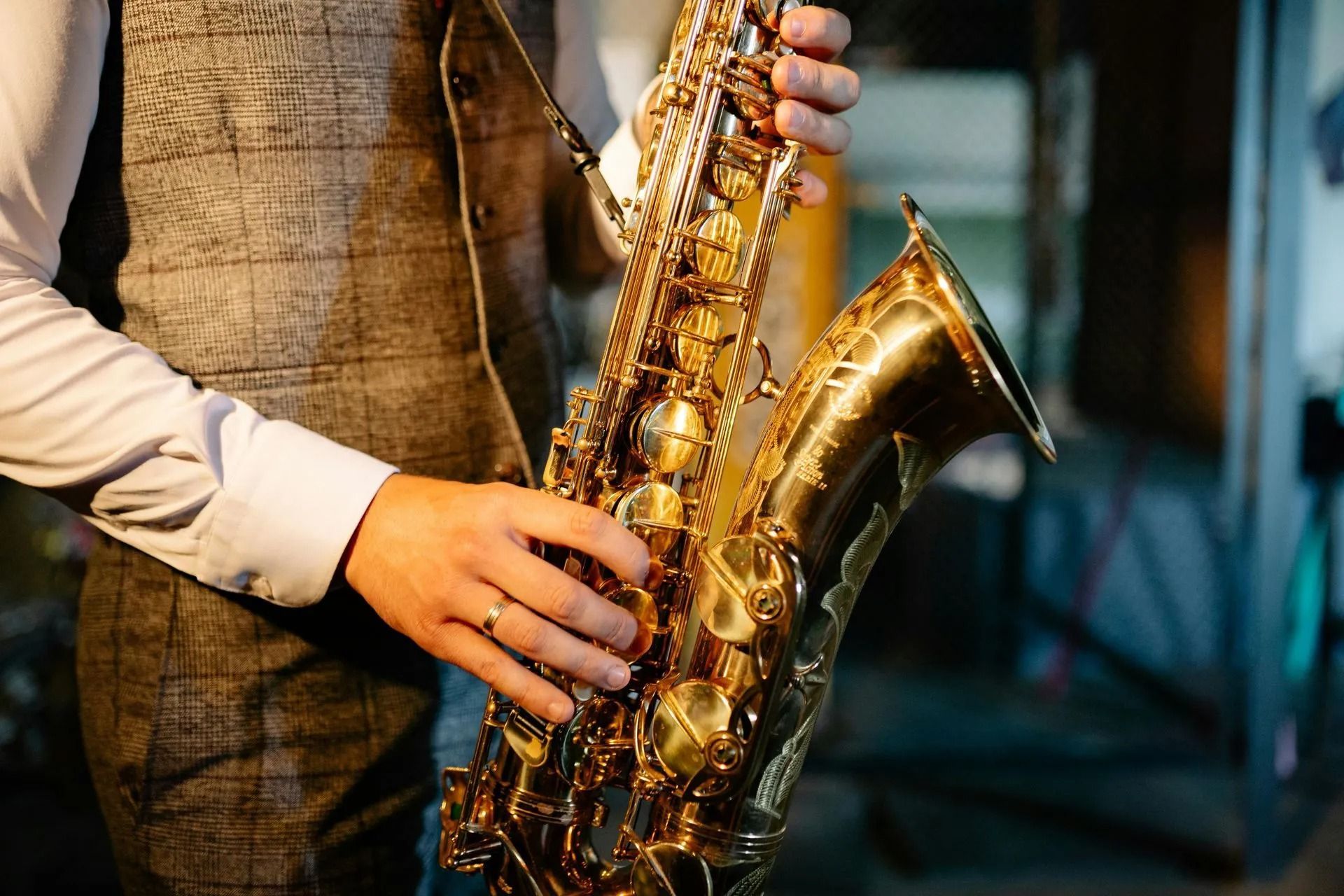 Person playing a gold saxophone on stage, wearing a vest and white shirt.
