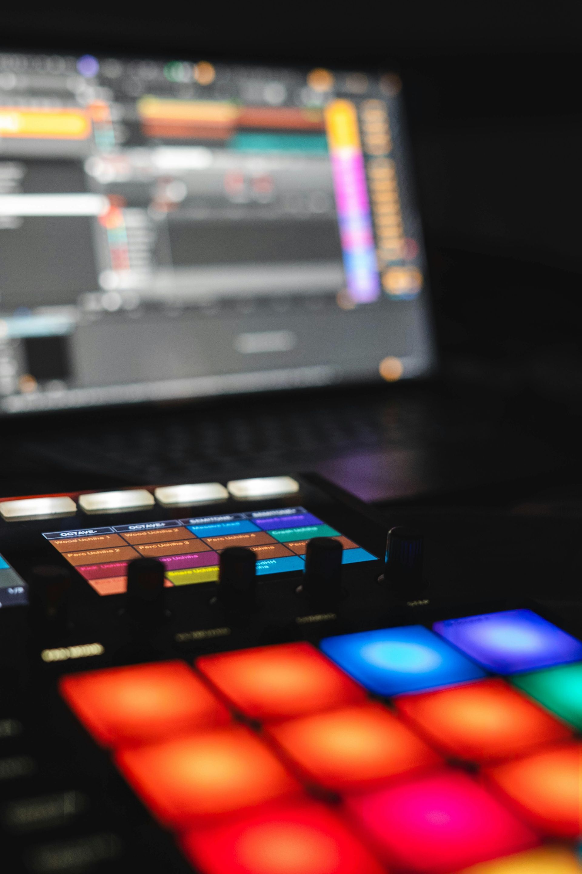 Colorful MIDI controller in foreground, with blurred music software displayed on a laptop screen behind it