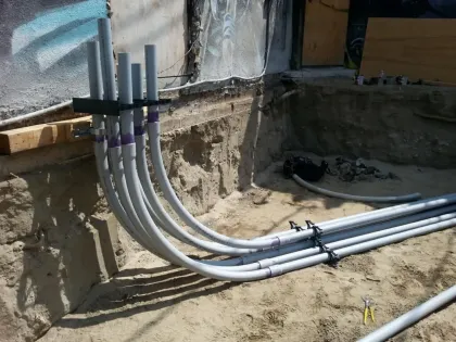 Construction site trench with gray electrical conduits entering a wall and running along the ground