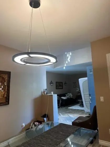 Modern dining room with a circular pendant light, neutral walls, and a view into a bedroom beyond.