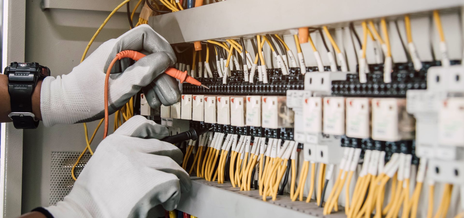 Gloved hands wiring an electrical control panel with orange and yellow cables