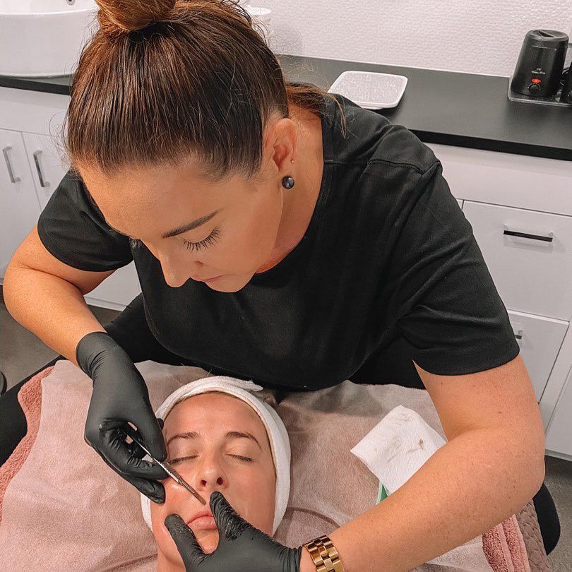 A Woman Wearing Black Gloves Is Applying A Cream To A Woman's Face — Beauty & Laser by Sarah in Long Jetty, NSW