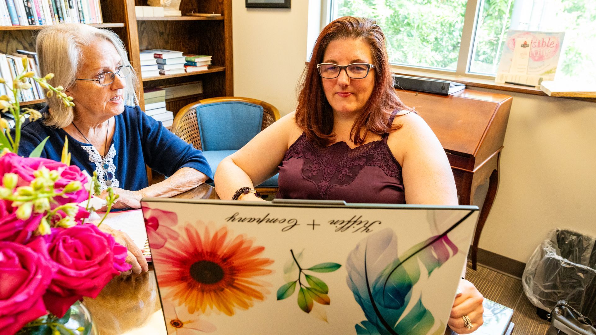 Two women are sitting at a table with a laptop.