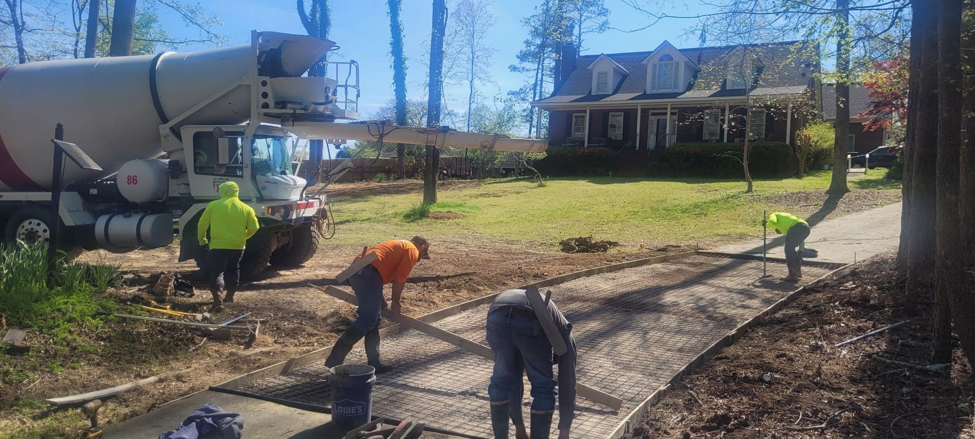 A group of construction workers are working on a driveway in front of a house.