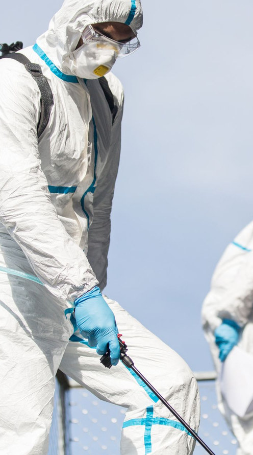 Persona in tuta protettiva che spruzza disinfettante. All'aperto, cielo azzurro.