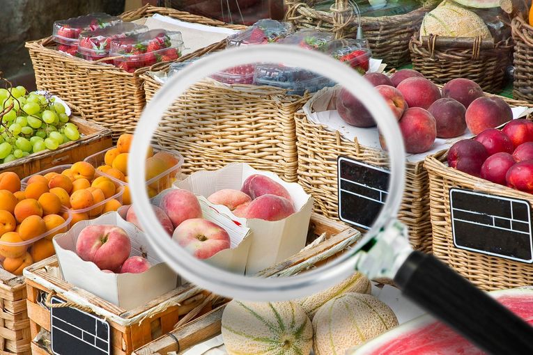 Lente d'ingrandimento sulle pesche esposte al mercato; altri frutti visibili nei cestini.
