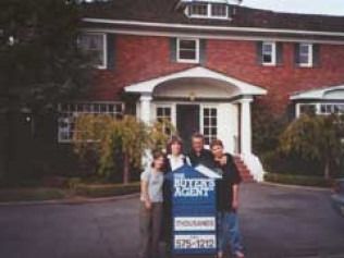 Person in wheelchair in front of a brick building with a garage, windows, and green lawn.