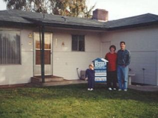 Family standing in front of a house, real estate sign in yard.