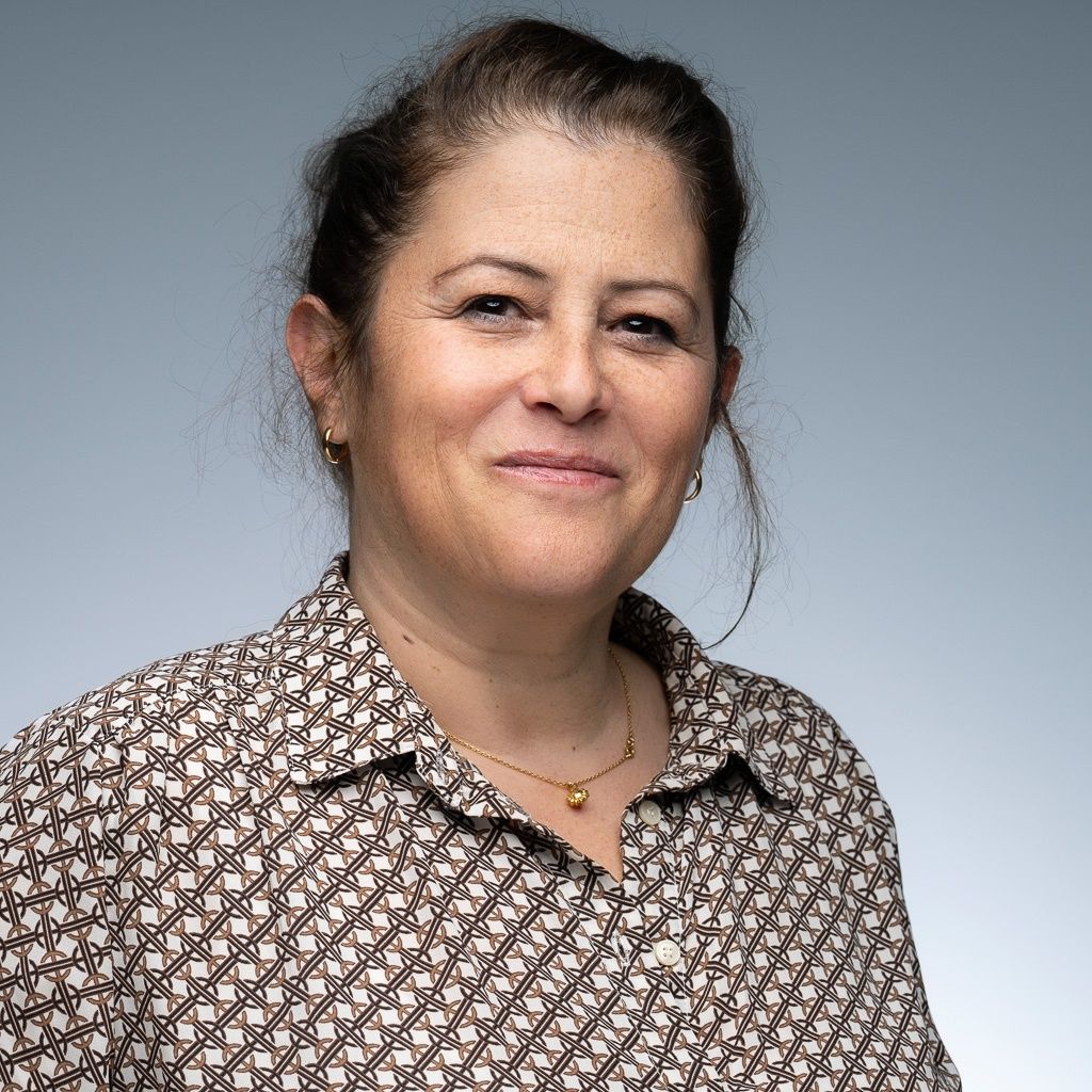 Une femme portant une veste blanche et une chemise verte sourit à la caméra