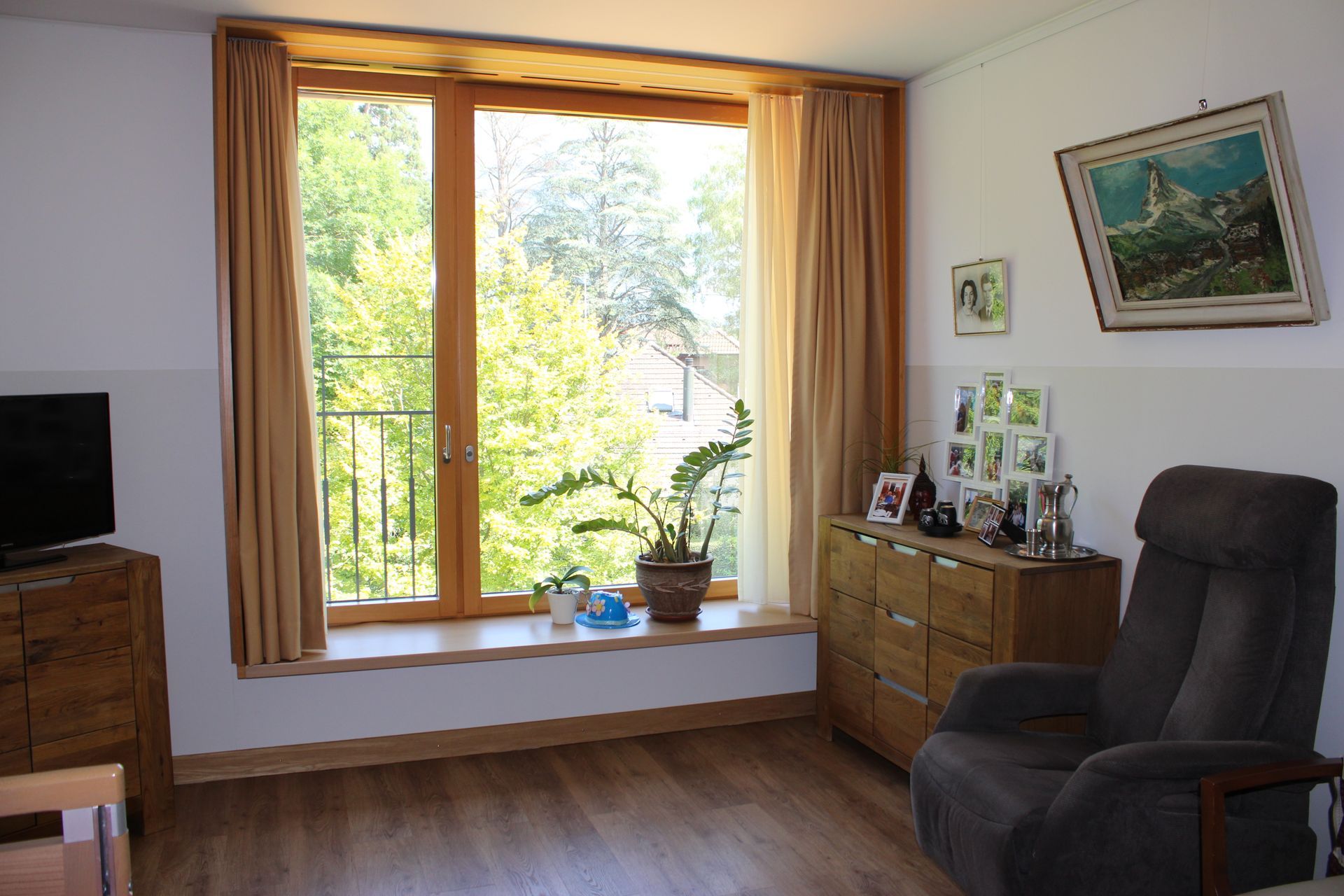 Un salon avec une chaise, une commode, une télévision et une grande fenêtre.