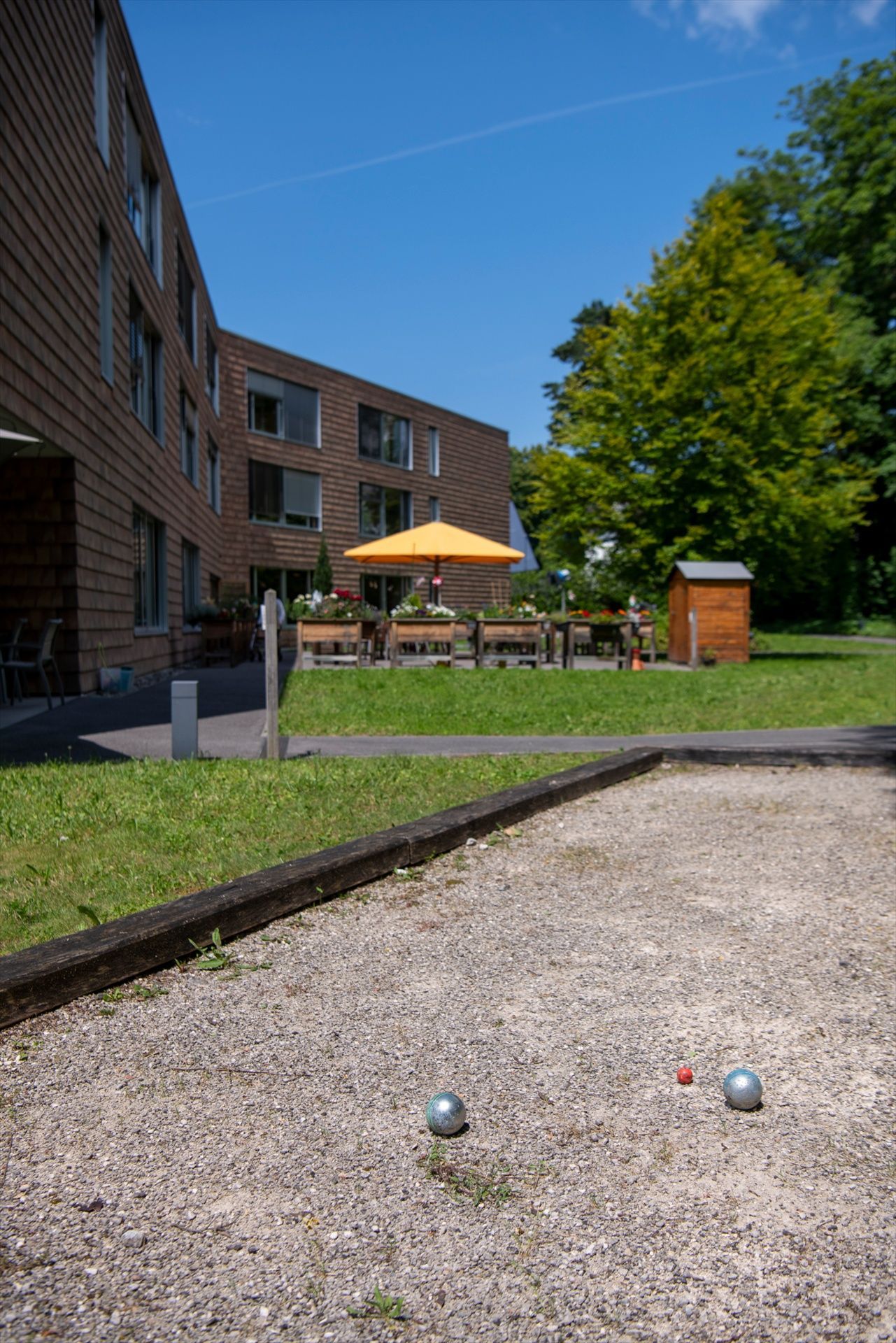 Un terrain de pétanque devant un bâtiment avec un grand bâtiment en arrière-plan.