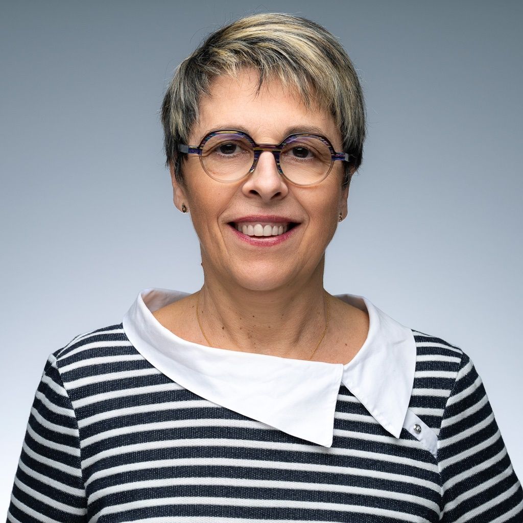 Une femme portant des lunettes et une chemise blanche sourit à la caméra.