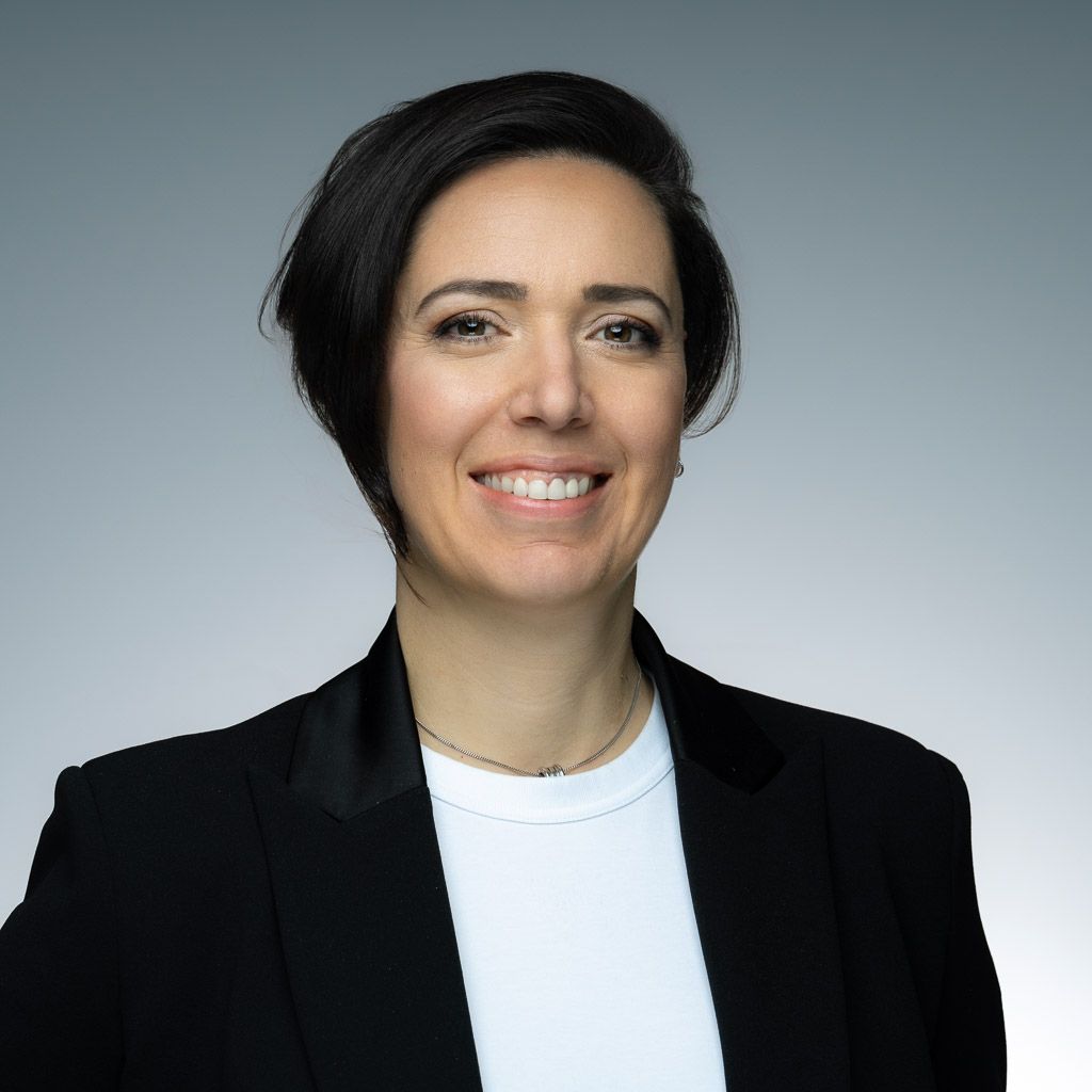 Une femme portant une veste noire et une chemise blanche sourit à la caméra.