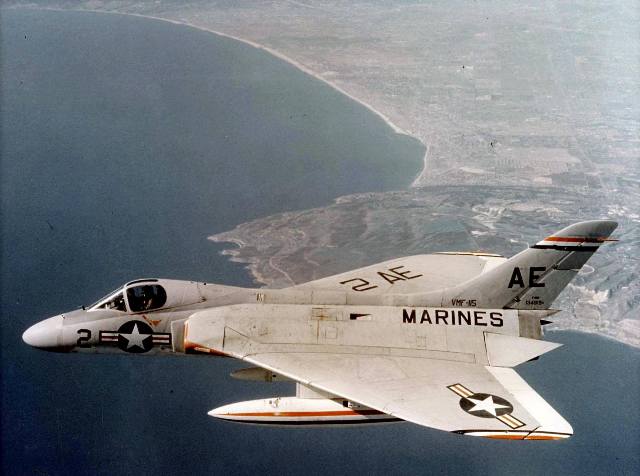 Marines F4D Skyray jet aircraft in flight over a coastline. Light grey with white and black markings.