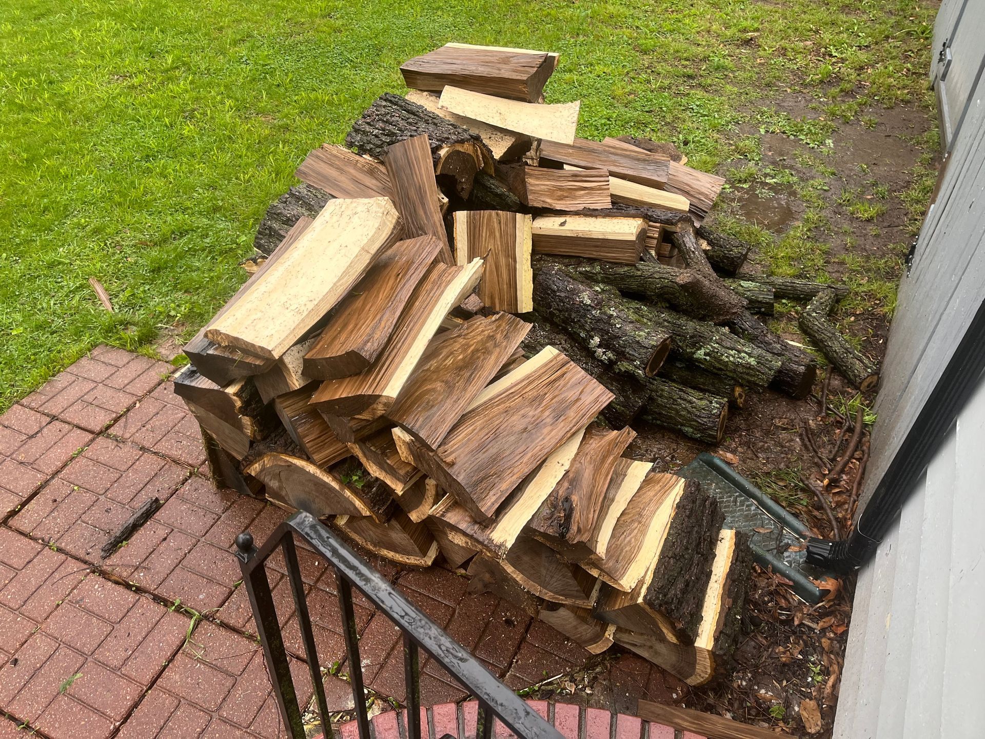 Pile of split firewood on brick and grass next to a house.
