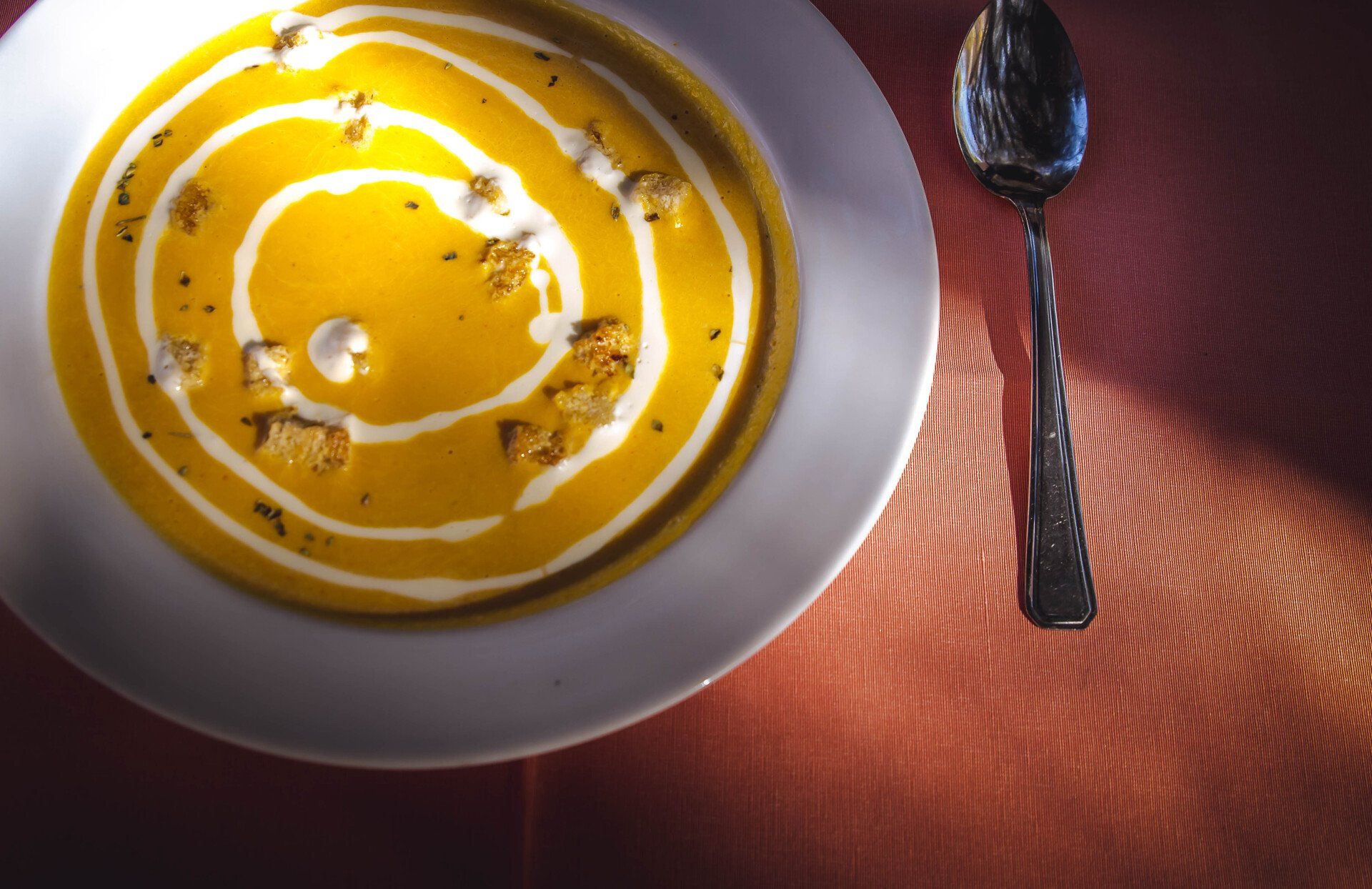Un plato de sopa junto a una cuchara sobre una mesa