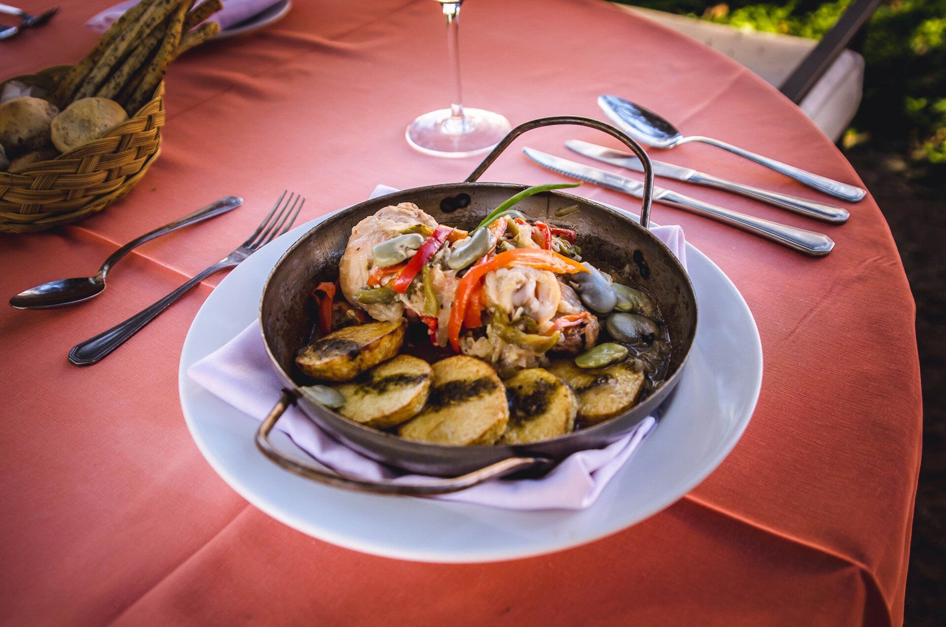 Un plato de comida sobre una mesa con utensilios y una copa de vino.