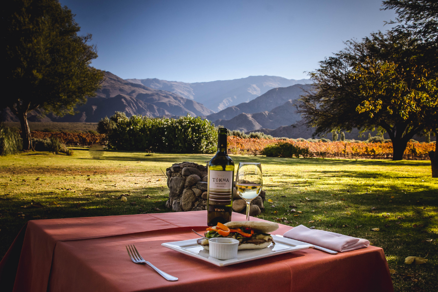 Una mesa con una botella de vino y un sándwich encima.