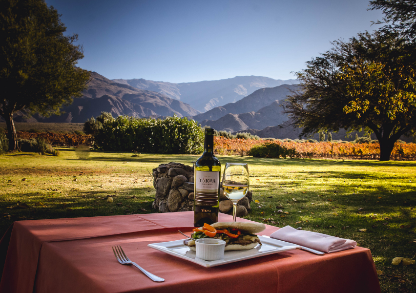 Una mesa con una botella de vino y un sándwich encima.
