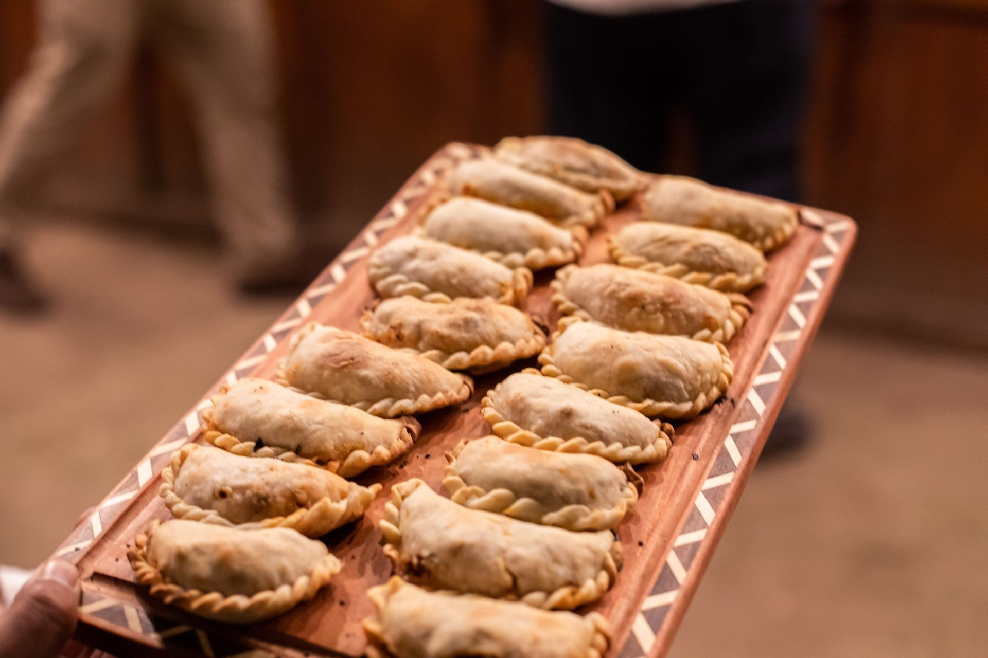 Una persona sostiene una bandeja de madera llena de empanadas.