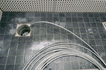 A drain cleaning snake coiled on a tiled shower floor, with the tip inserted into the open drain.