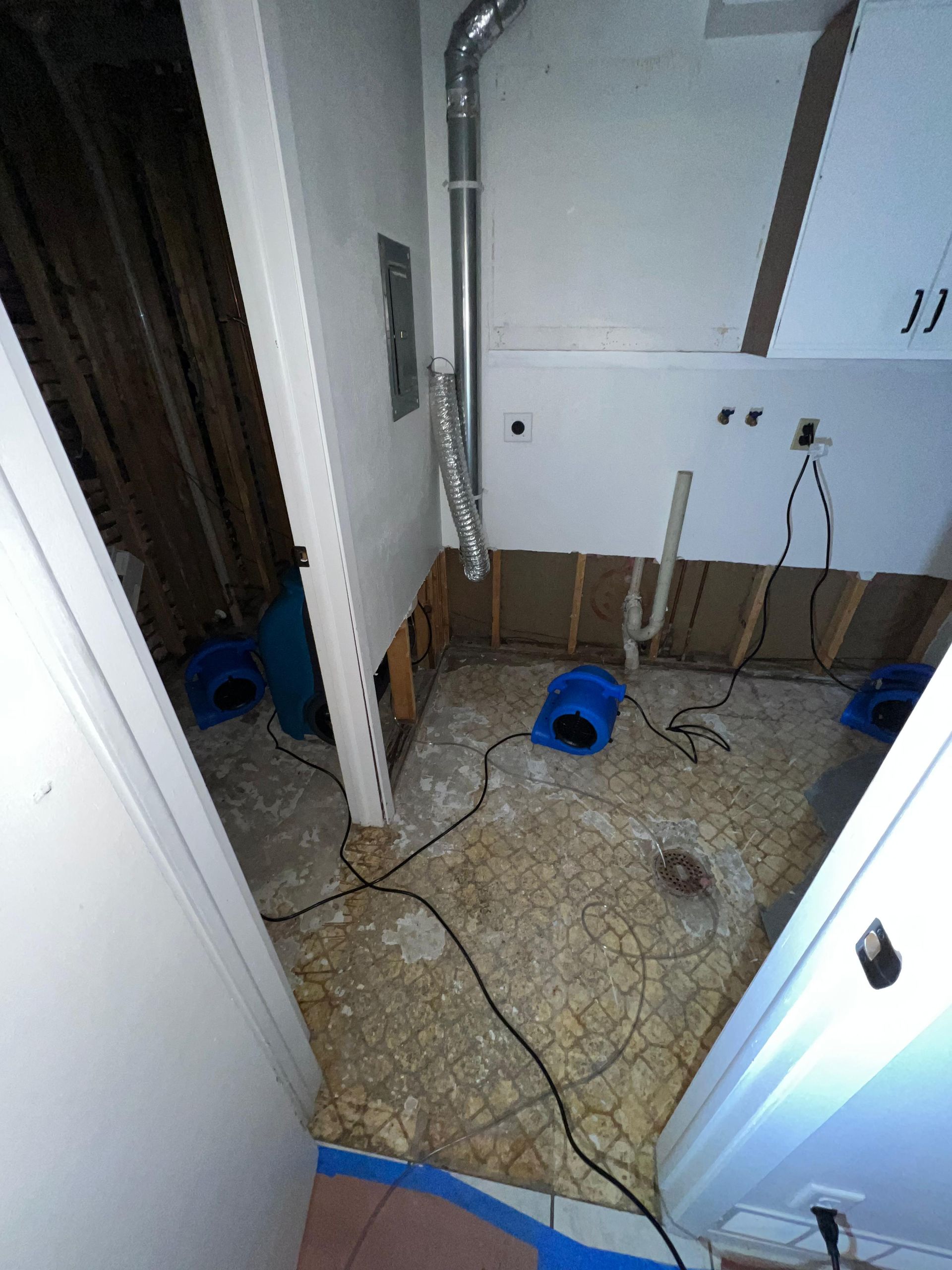 Small unfinished room with exposed wires, blue tool, and cabinet; floor covered with cables and debris.