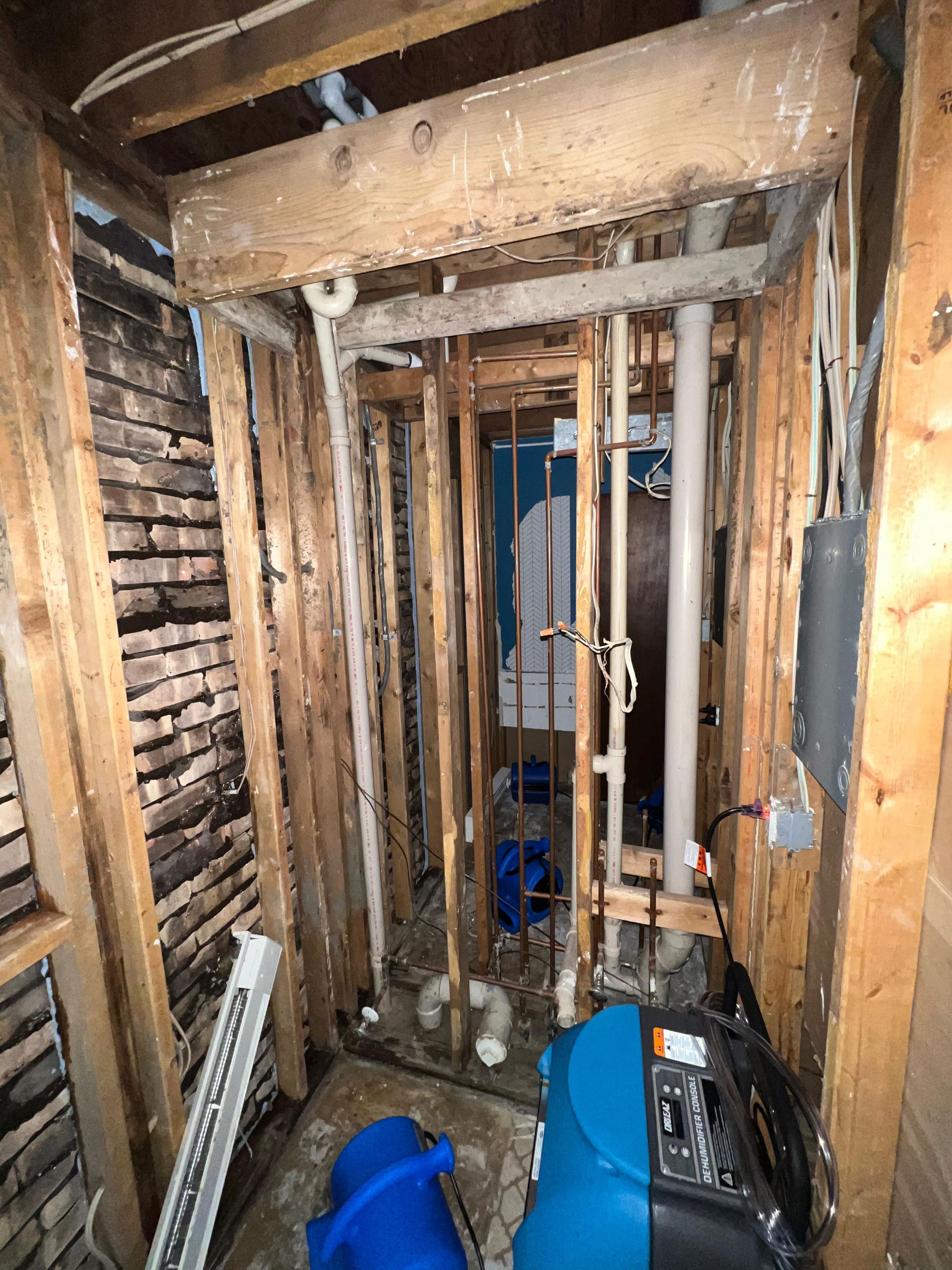 Damaged interior wall with exposed studs, pipes, and debris in a narrow renovation area