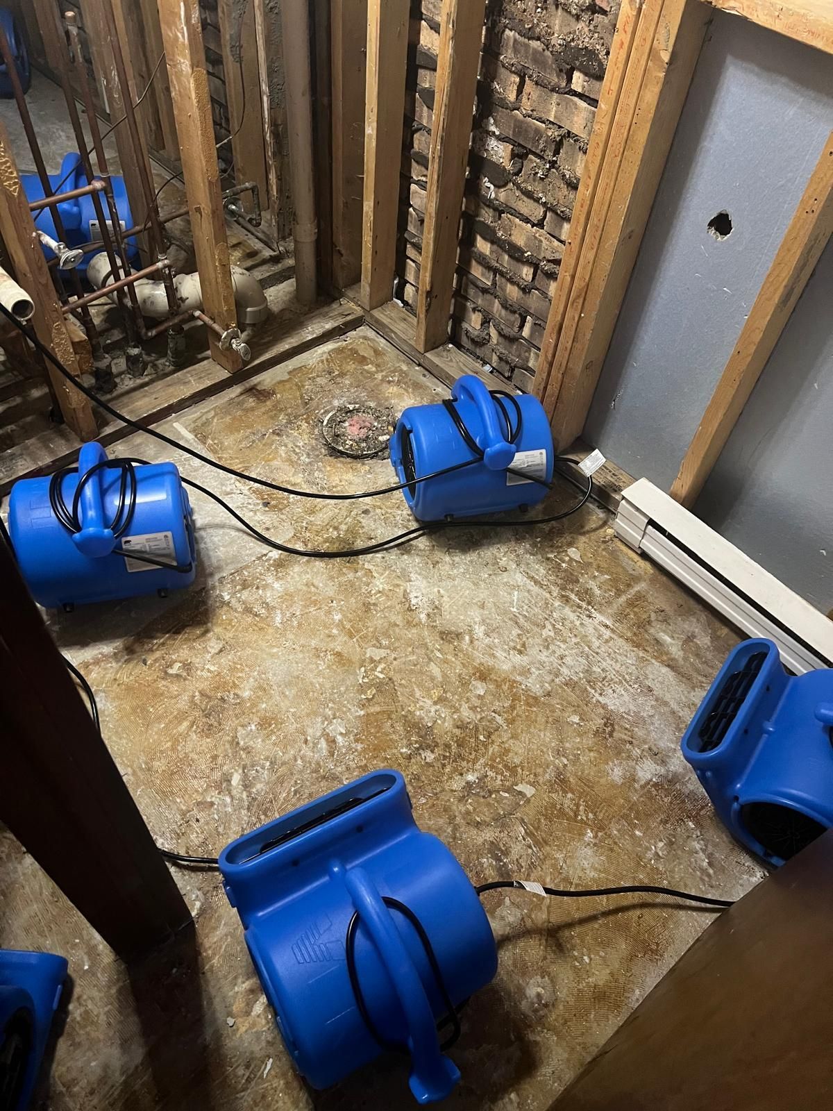 Flood-damaged room with blue air movers drying the floor and exposed wall framing