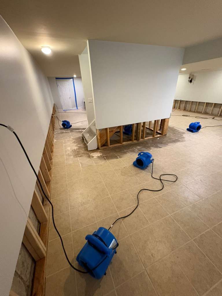 Basement under renovation with blue fans, exposed framing, and a cord on the floor