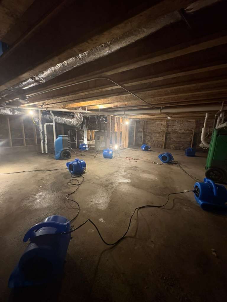 Basement under renovation with blue fans, exposed beams, and cords on the concrete floor
