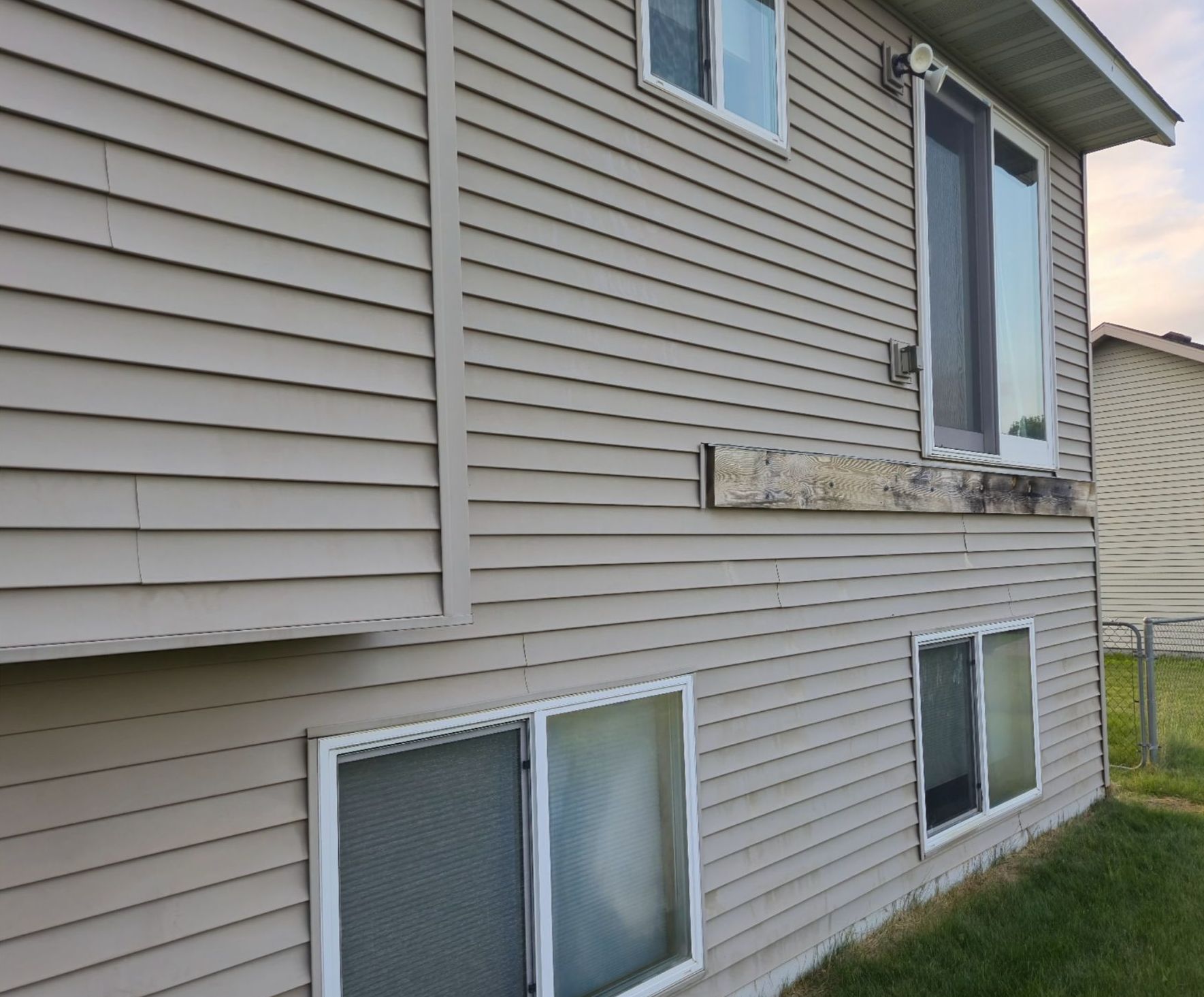Tan siding on a two-story house with a sliding glass door on the upper level and windows on both levels.
