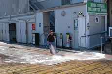 Man sprays down a dock with soapy water, near a building with a green sign that reads 
