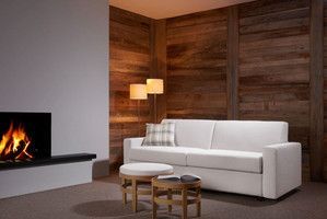 ein weißes Schlafsofa steht auf einem Holzboden vor einer Holzwand bei einem Kaminfeuer.