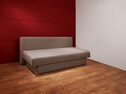 In einem Raum mit einer roten Wand steht ein Sofa ohne Polster.