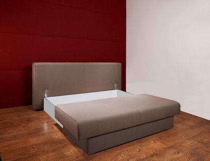 In einem Raum mit roter Wand steht ein ausgezogenes Sofa auf einem Holzboden.