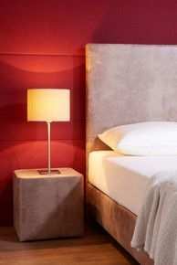 Ein Schlafzimmer mit Bett und gräulichem Kopfteil, Nachttisch, Lampe und roten Wänden.