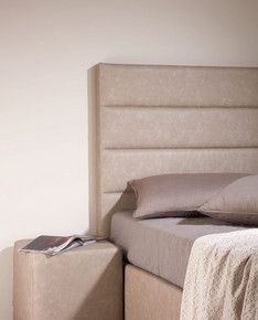 Ein Bett mit grauem Kopfteil  und grauen Polstern.