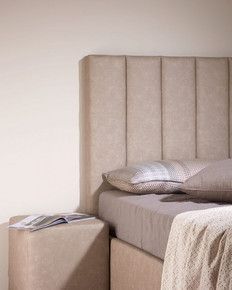 Ein Bett mit grauem Kopfteil und einem Nachttisch daneben.