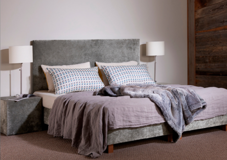 Ein Bett mit grauem Kopfteil und Kissen in einem Schlafzimmer.