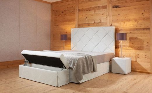 Ein Schlafzimmer mit einem Bett mit zugehörigem Kopfteil und Stauraum vor einer Holzwand.