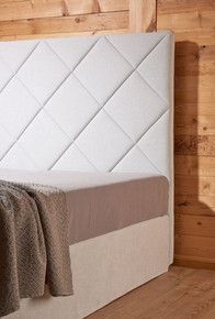 Ein Bett mit einem weißen Kopfteil und einer braunen Decke darauf.