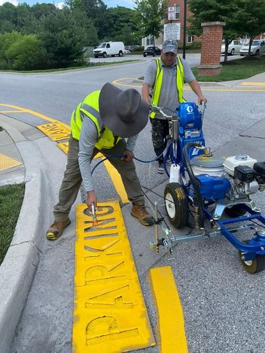 Two workers in yellow safety vests spray-paint the word 