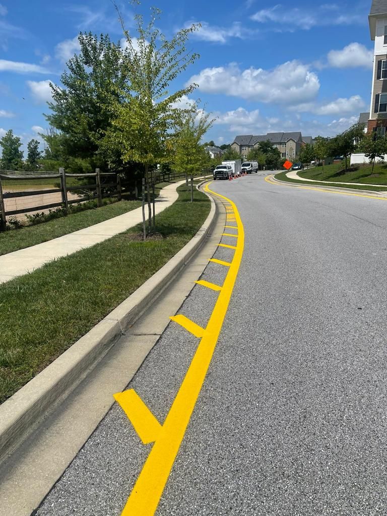 A suburban street with a curb painted with a solid yellow line and perpendicular yellow hash marks on the asphalt.