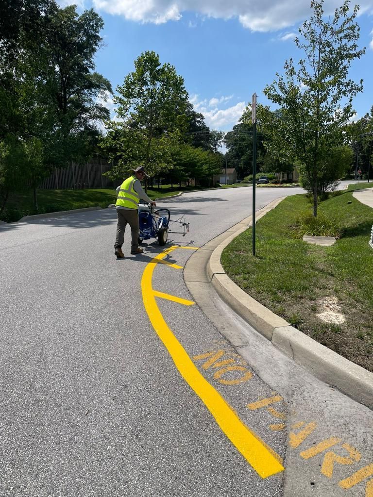 A worker in a yellow safety vest uses a walk-behind machine to paint