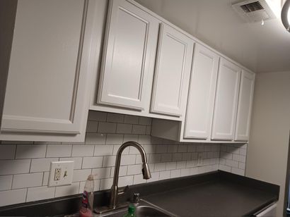 White kitchen cabinets mounted above a sink with a dark countertop and a white subway tile backsplash.