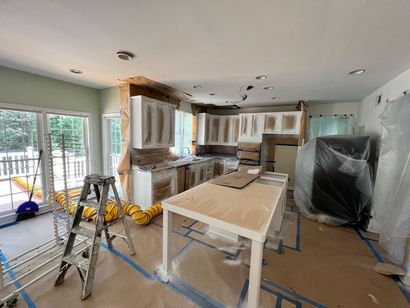 A kitchen interior during a renovation, featuring masked cabinets, a central island, and floor protection tape.