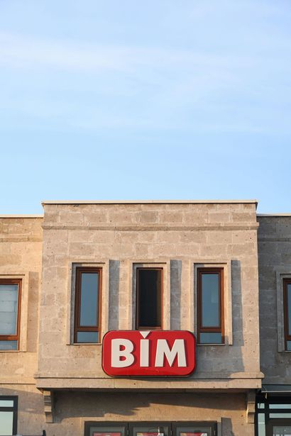 A stone building facade with three windows and a red-and-white BIM grocery store sign centered below the middle window.