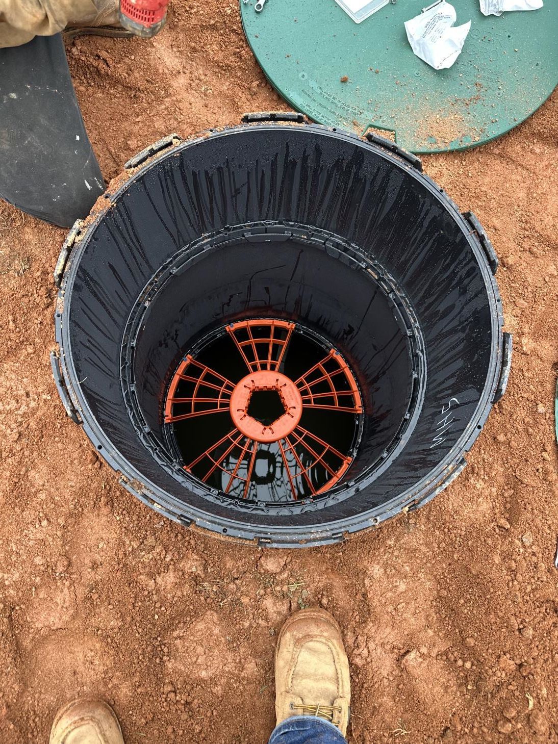 A person is standing in the dirt next to a bucket filled with water.