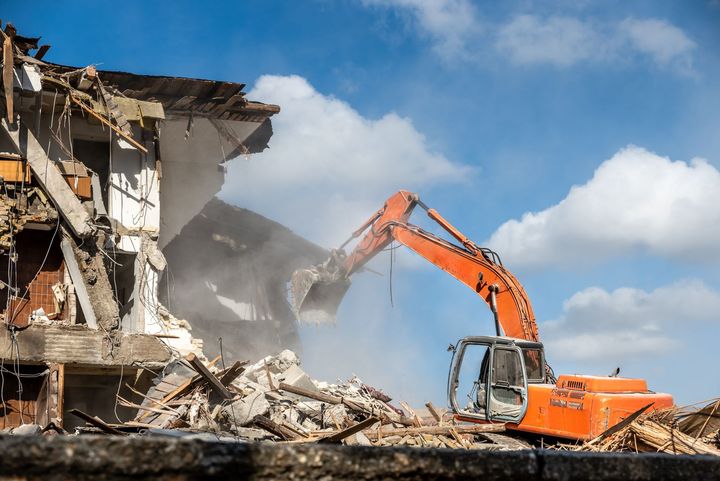 A large orange excavator is demolishing a building.